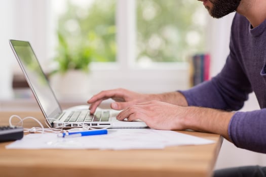 Close up low angle view of a man working from home on a laptop computer sitting at a desk surfing the internet